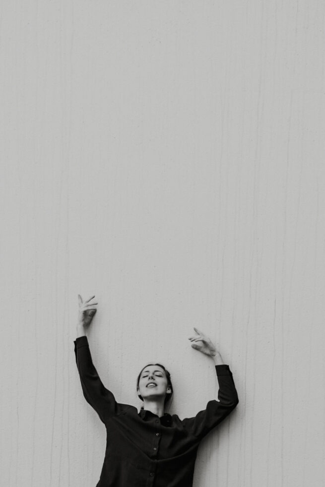 A woman with her hands up in black and white photography by Monica Juno